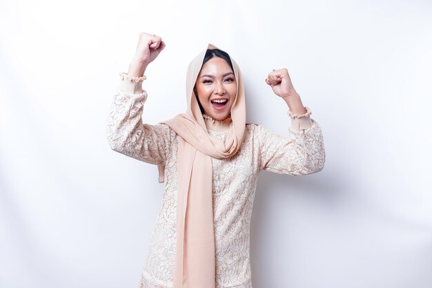 A young Asian Muslim woman with a happy successful expression wearing a hijab isolated by white background