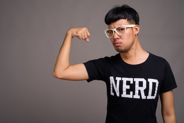 Young Asian nerd man wearing eyeglasses against gray