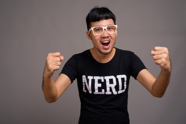 Young Asian nerd man wearing eyeglasses against gray