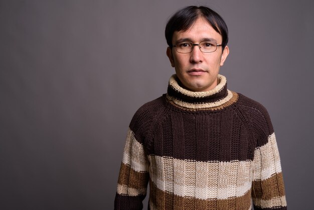 Young Asian nerd man wearing turtleneck sweater against gray wall