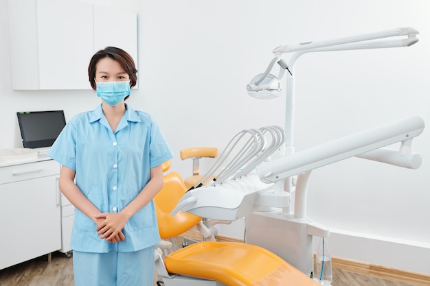 Young asian nurse in medical mask standing in office of dental
clinic