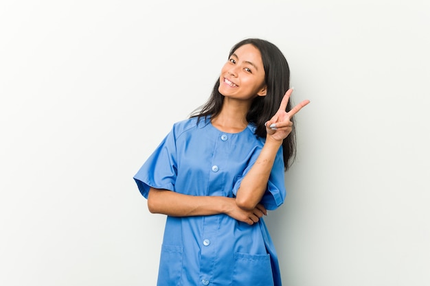 Young asian nurse woman joyful and carefree showing a peace symbol with fingers.