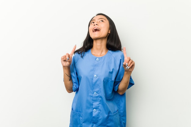 Young asian nurse woman pointing upside with opened mouth.