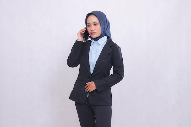 A young Asian office executive woman wearing a hijab stands elegantly while calling someone on her c