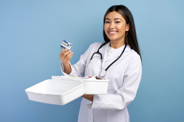 Young asian paramedic in white uniform holding opening box with medicine and smiling