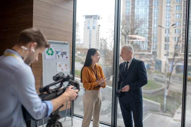 Young asian reporter in beige pants having a conversation with a grey-haired man