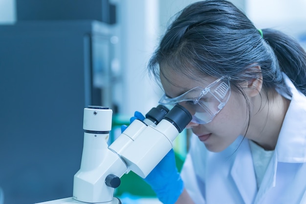 実験室で顕微鏡を通して見ている若いアジアの科学者いくつかの研究をしているタイの人々