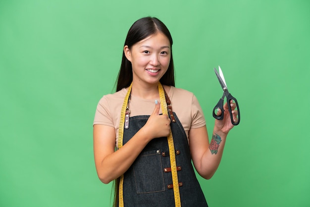 親指を立てるジェスチャーを与える孤立した背景の上の若いアジアの裁縫師の女性