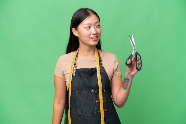 Young Asian seamstress woman over isolated background looking to the side and smiling