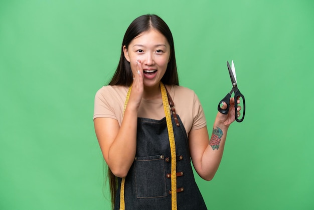 Young Asian seamstress woman over isolated background shouting with mouth wide open