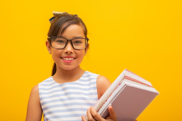 黄色の背景に本を持って若いアジア学生の女の子