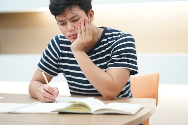 Stress studente giovane uomo asiatico durante la lettura e fare pre-test dell'esame