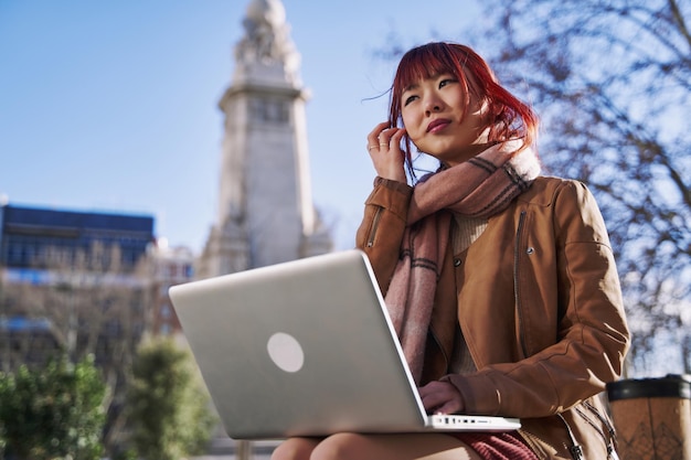 Young asian student sitting on campus using her laptop outdoors