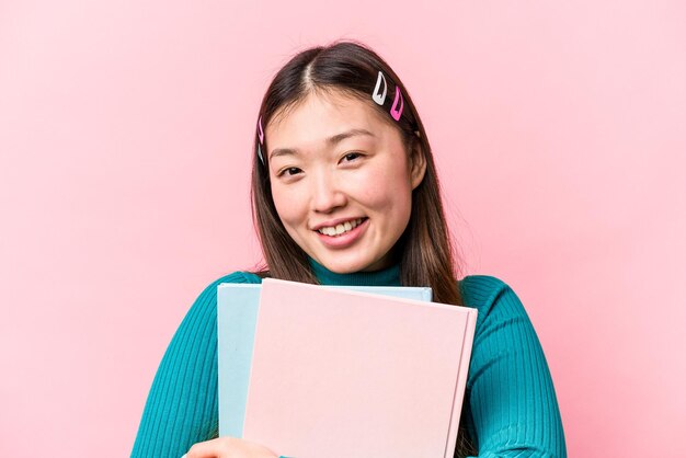 Young asian student woman holding books isolated on pink background