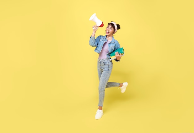 Young Asian student woman shouting into megaphone making announcement in isolated on yellow background.