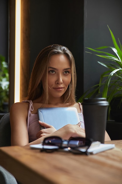 Young asian stylish pretty woman sitting at table of coffee shop holding laptop