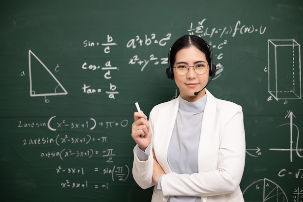 Giovane insegnante asiatica che tiene il gesso per insegnare la videoconferenza con lo studente insegnante femminile che addestra la matematica nel corso online di lavagna in classe