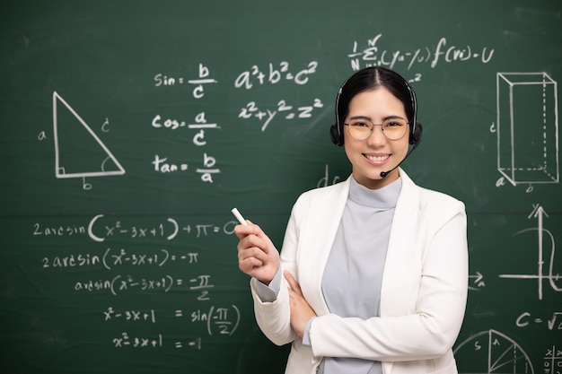 Giovane insegnante asiatica che tiene il gesso per insegnare la videoconferenza con lo studente insegnante femminile che addestra la matematica nel corso online di lavagna in classe