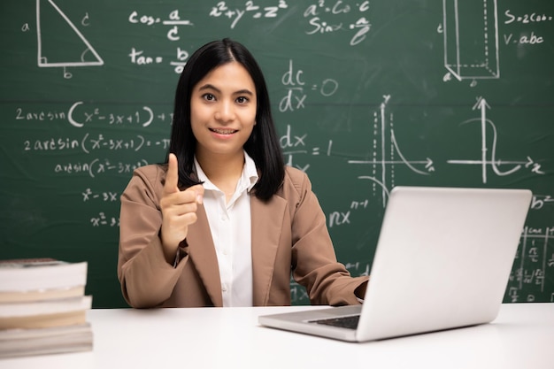 젊은 아시아 교사 여성 학생과 노트북 화상 회의를 사용하여 앉아 컴퓨터 온라인 과정으로 라이브 스트림에서 교실에서 수학을 훈련하는 여교사