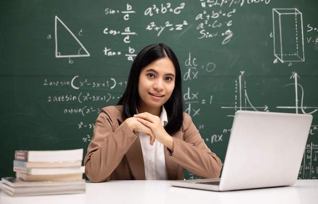 Young asian teacher woman sitting using laptop video conference\
with student female teacher training the mathematics in classroom\
from live stream with computer online course