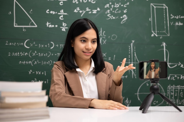 Young asian teacher woman sitting and video conference with student Female teacher training the mathematics in classroom from live stream with smartphone online course