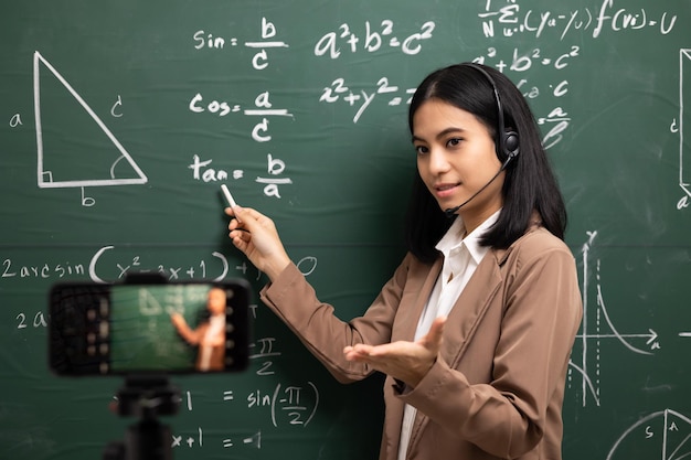 Young asian teacher woman standing looking at camera and video
conference with student female teacher training the mathematics in
classroom from live stream with smartphone online course