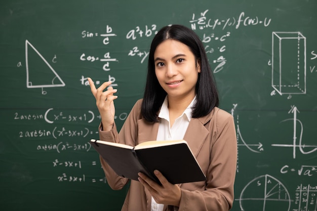 Giovane insegnante asiatica che insegna a tenere libro e videoconferenza con la fotocamera degli studenti insegnante femminile che forma la matematica in classe lavagna dal corso online