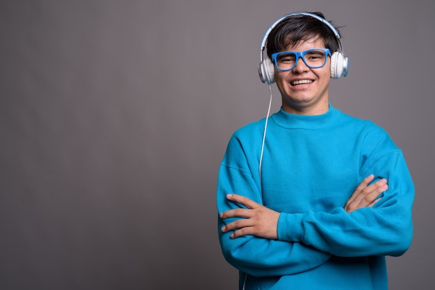 Young Asian teenage boy listening to music against gray backgrou