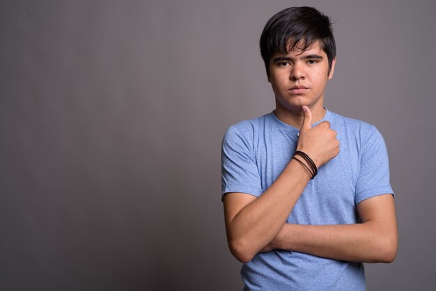 Young Asian teenage boy wearing blue shirt against gray wall