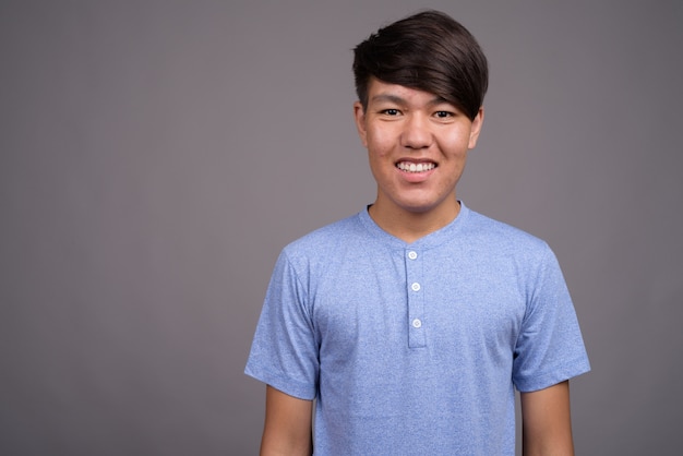 young Asian teenage boy wearing blue shirt against gray wall