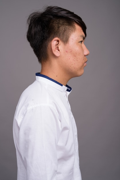 young Asian teenage boy wearing smart casual clothes against gray wall