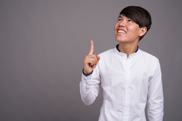 young Asian teenage boy wearing smart casual clothes against gray wall