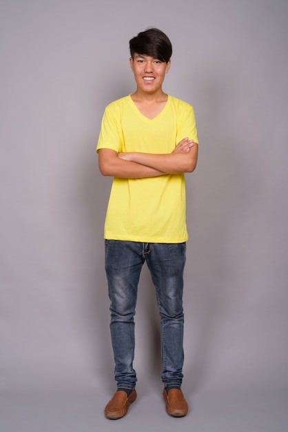 young Asian teenage boy wearing yellow shirt against gray background