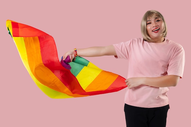 Молодой азиатский трансгендер ЛГБТ с радужным флагом изолирован на фоне розового цвета Гендерное выражение гордости и концепции равенства