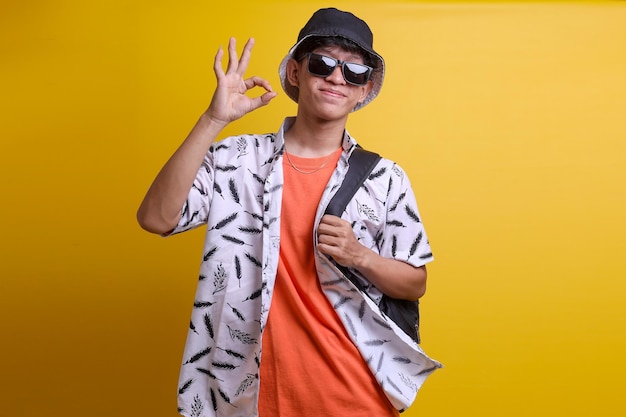 Young asian traveler man in casual clothes and sunglasses showing ok sign and smiling over isolated