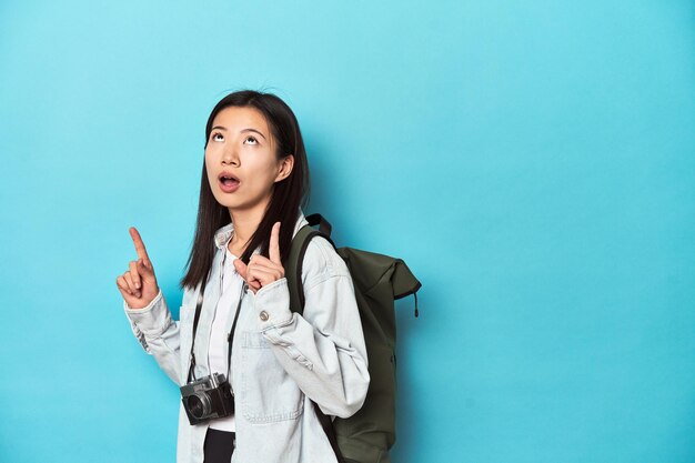 Young Asian traveler ready to capture adventures pointing upside with opened mouth