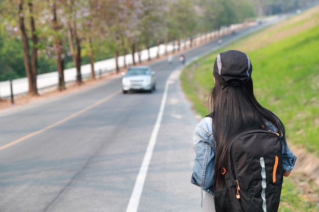 Молодой азиатский путешественник с автомобилем рюкзака ждать на дороге пока путешествующ во время праздничных каникул
