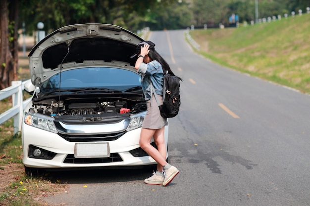 バックパックを持つ若いアジア旅行者の女性は車が壊れて助けを待ってしまった