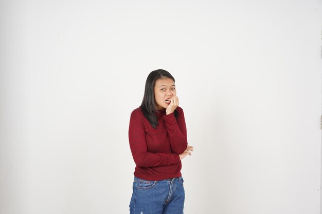 白い背景に孤立した赤いTシャツを着た若いアジア人女性が怖がって爪をみます