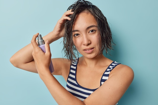 Young asian woman applies conditioner mask on wet hair after
taking shower enjoys spa and wellness dressed in striped t shirt
iolated over blue background women cosmetology and hair care
concept