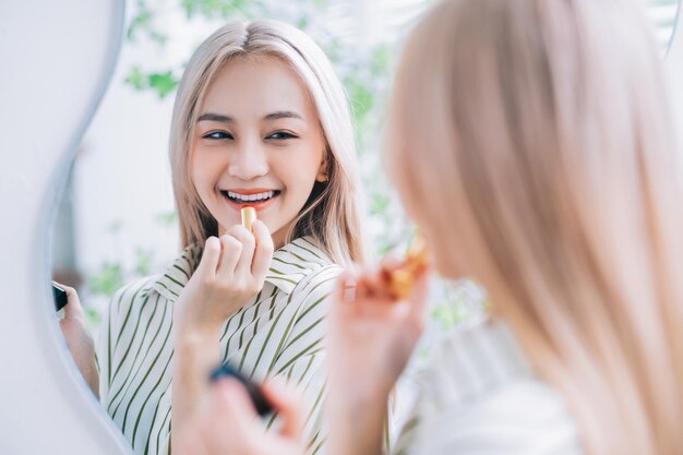 Young Asian woman applying lipstick in front of mirror