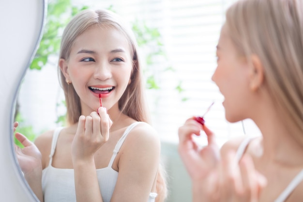 Young Asian woman applying lipstick in front of mirror