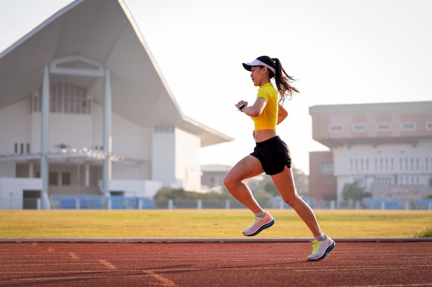 フィットネスと健康的なライフスタイルを維持するために、晴れた朝に市のスタジアムのランニングトラックでジョギングしている若いアジアの女性アスリートランナー。若いフィットネス女性がスタジアムのトラックを実行します。スポーツとレクリエーション