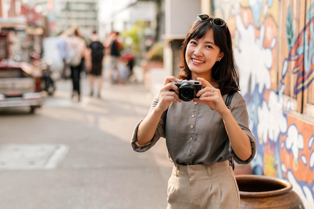 젊은 아시아 여성 배낭여행자는 디지털 컴팩트 카메라를 사용하여 거리 문화 지역 장소를 즐기고 옆길을 확인하는 여행자
