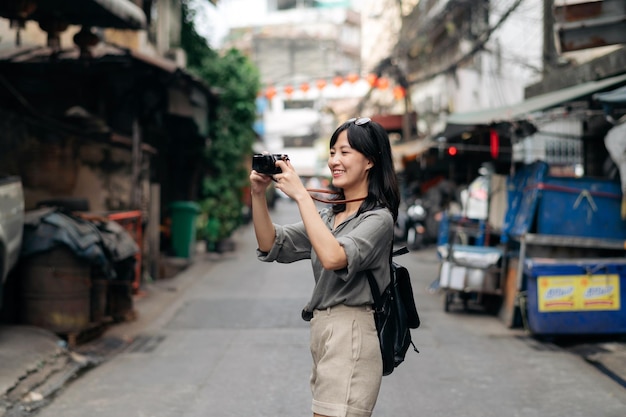 Young Asian woman backpack traveler using digital compact camera enjoying street cultural local place and smile