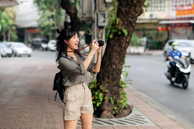 Young Asian woman backpack traveler using digital compact camera enjoying street cultural local place and smile