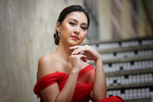 Молодая азиатская женщина в красивом красном платье, глядя на камеру с улыбкой. Фотомодель, невеста или предсвадебная концепция.