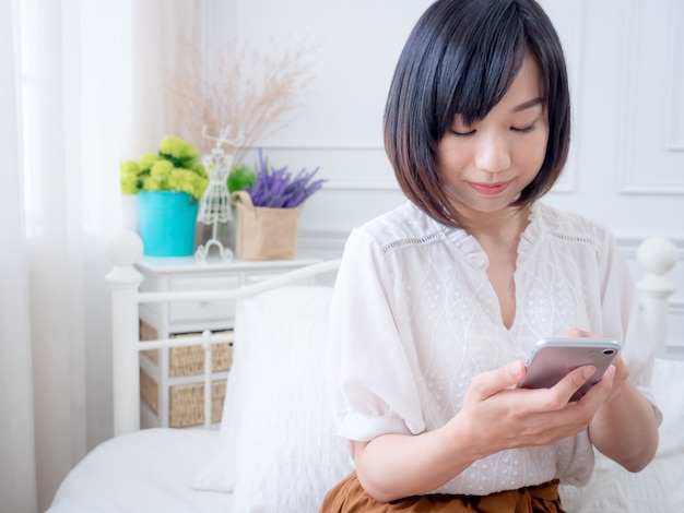Молодая азиатская женщина на кровати с помощью телефона