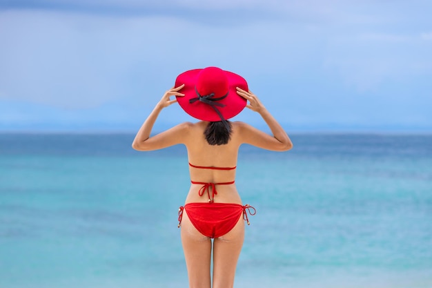 Giovane donna asiatica in bikini con il cappello che sta sulla vacanza estiva della spiaggia phuket thailand