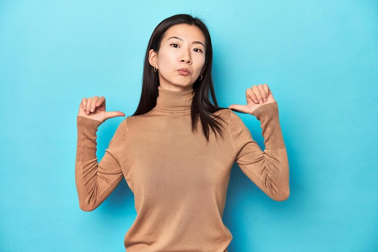 Photo 갈색 터틀넥을 입은 젊은 아시아 여성은 자랑스럽고 자신감 넘치는 모범을 보입니다.